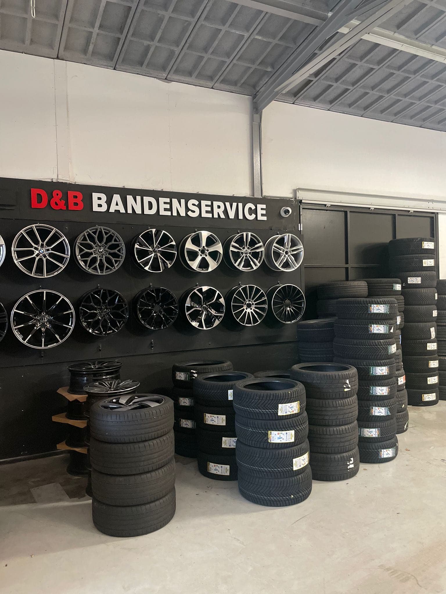 Wand vol lichtmetalen velgen en stapels banden onder het bord D&B Bandenservice in de werkplaats in Rotterdam