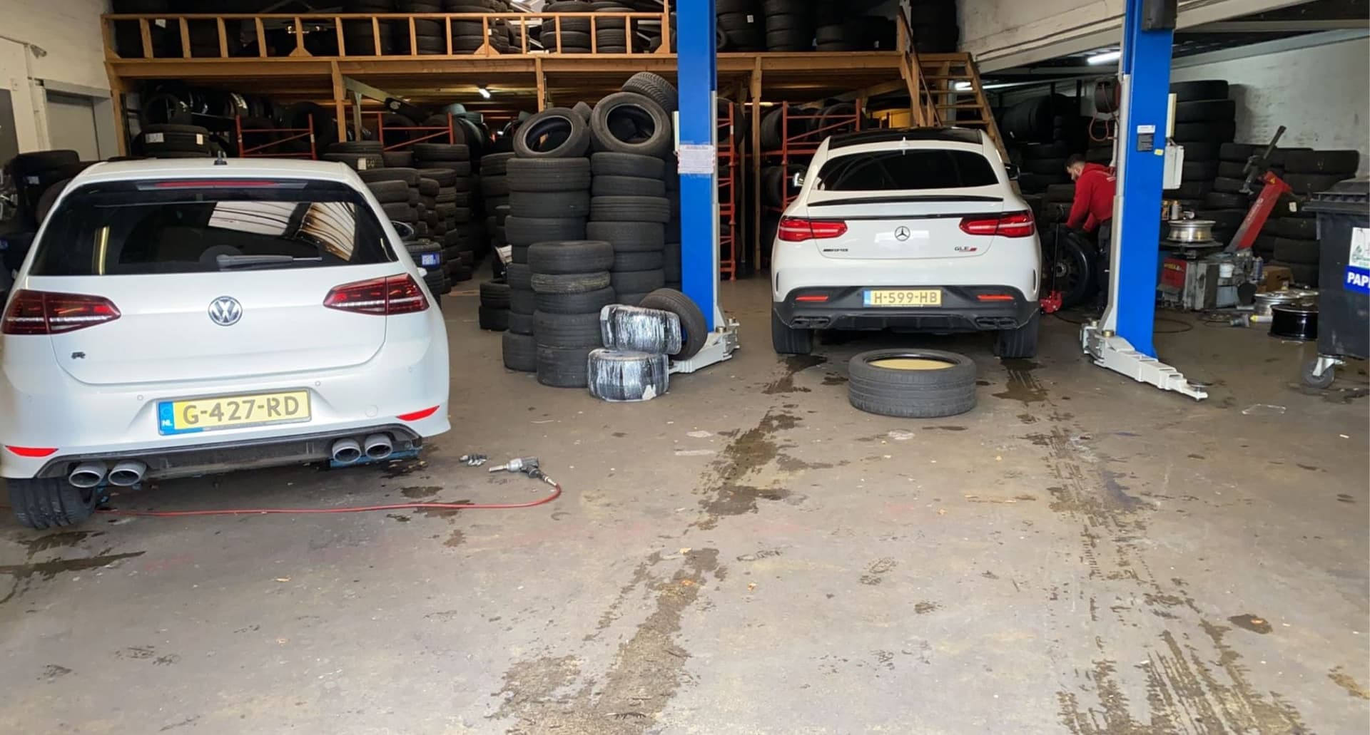 Twee auto's naast elkaar in de werkplaats met stapels banden langs de muur