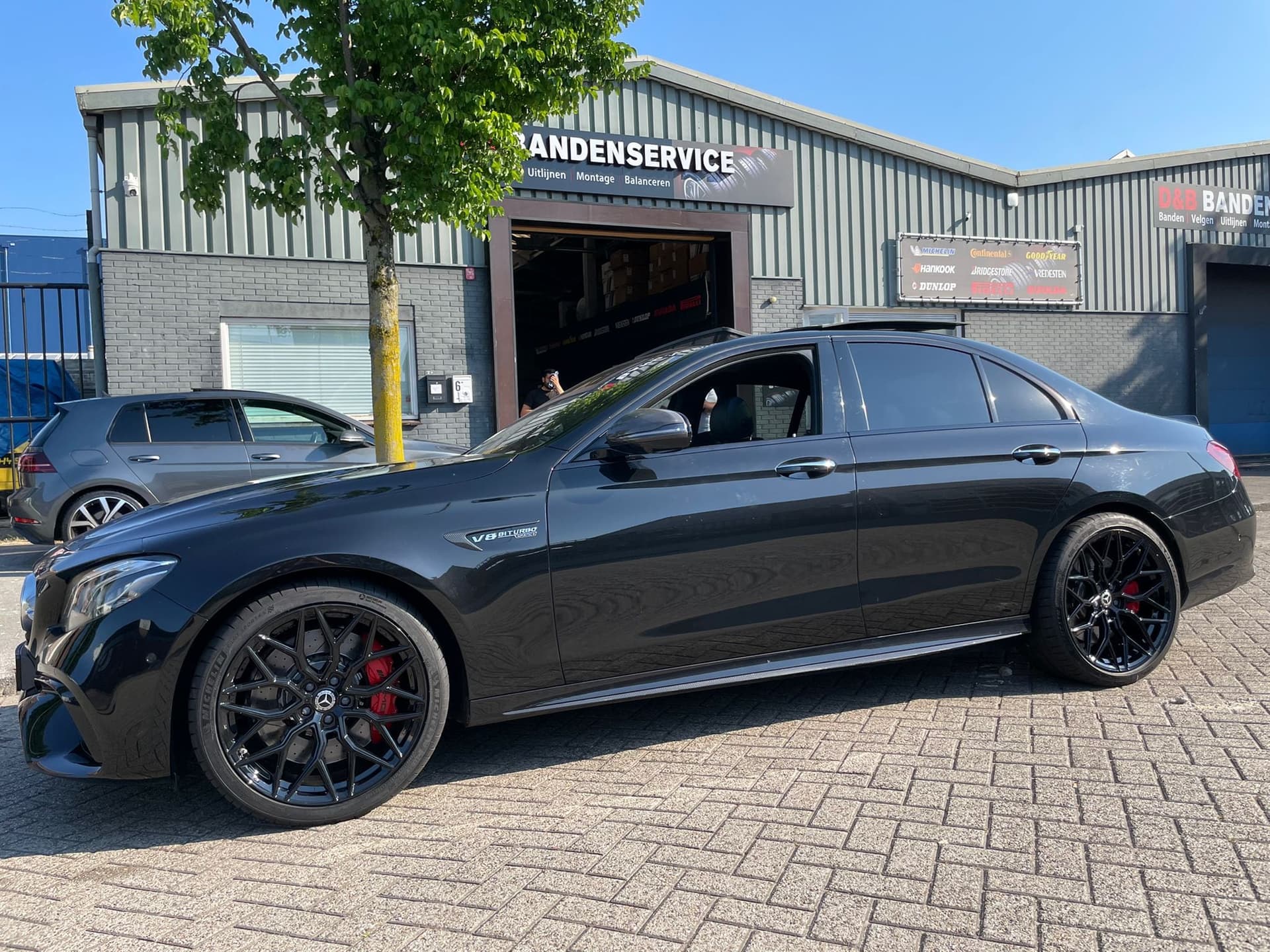Een donkergrijze Mercedes AMG met zwarte velgen voor het pand van D&B Bandenservice
