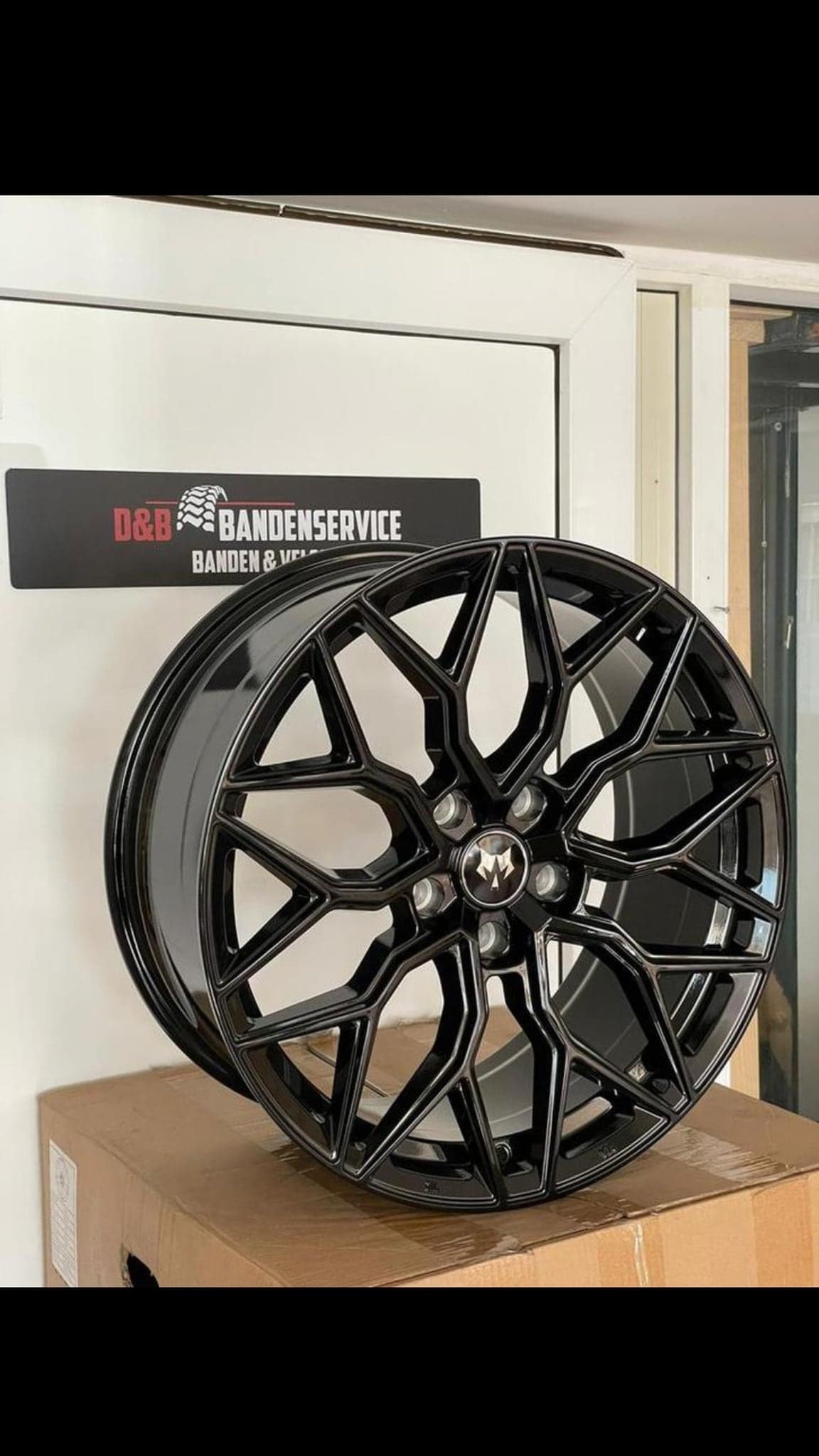 Nieuwe zwarte lichtmetalen velg onder het bord D&B Bandenservice banden en velgen